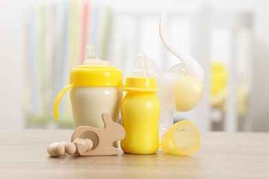 Photo of Feeding bottles with milk, breast pump and toy on wooden table indoors