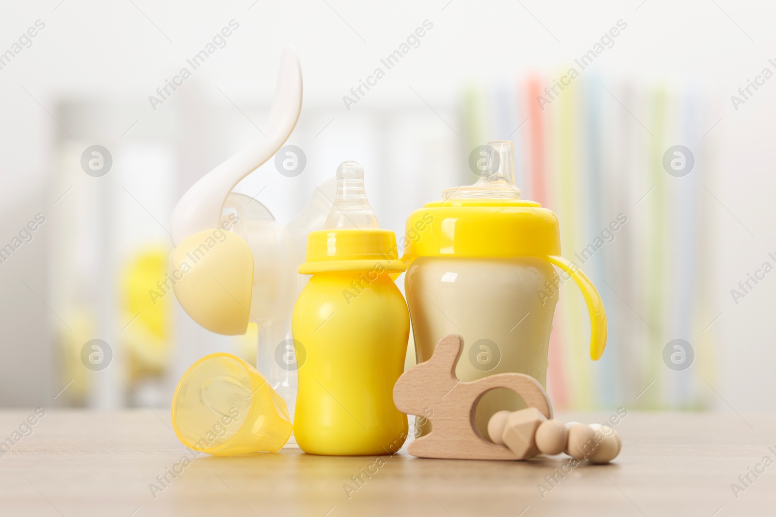 Photo of Feeding bottles with milk, breast pump and toy on wooden table indoors