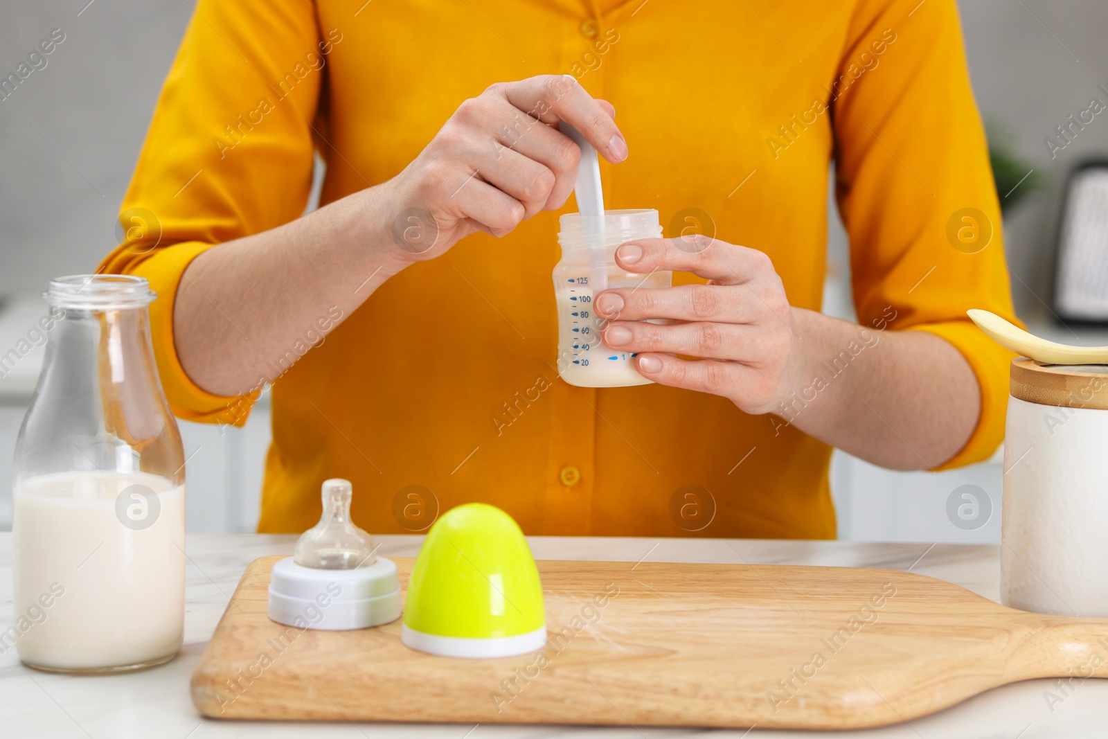 Photo of Mother making baby formula in feeding bottle at table indoors, closeup