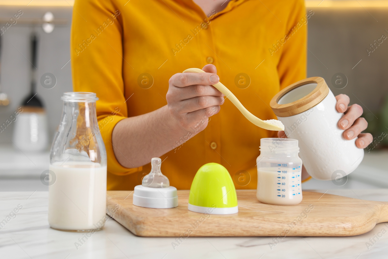 Photo of Mother making baby formula in feeding bottle at table indoors, closeup