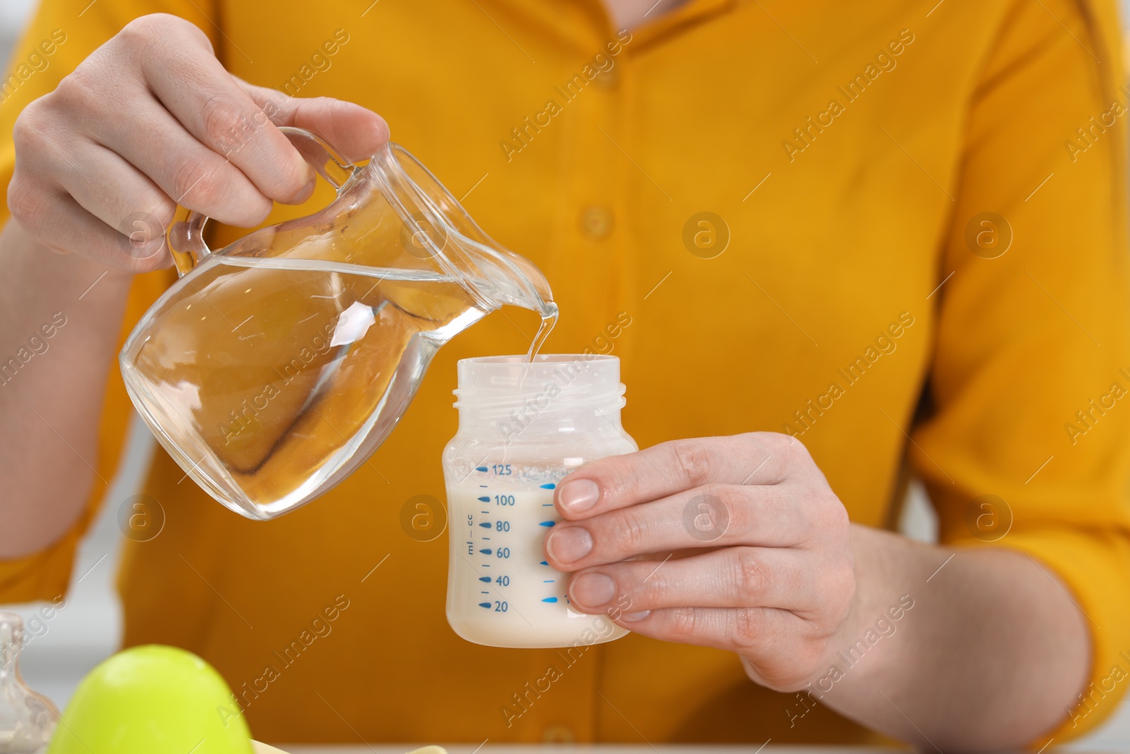 Photo of Mother making baby formula in feeding bottle indoors, closeup