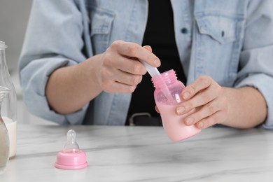 Photo of Mother making baby formula in feeding bottle at table indoors, closeup