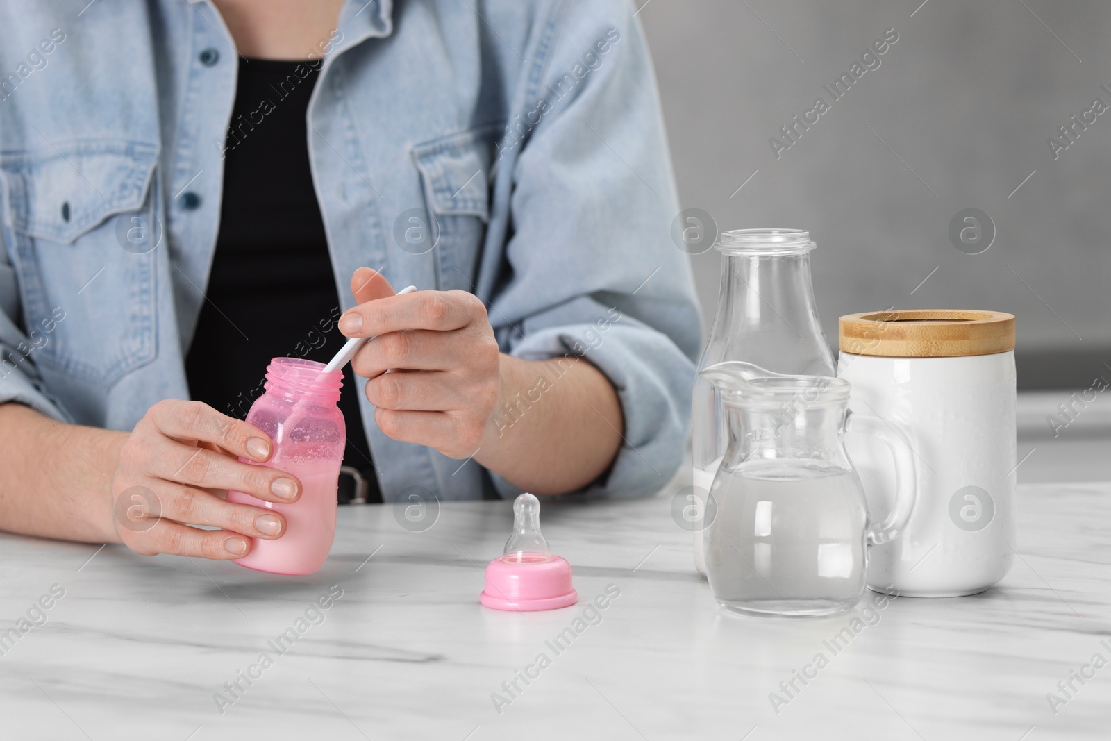 Photo of Mother making baby formula in feeding bottle at table indoors, closeup