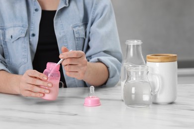 Photo of Mother making baby formula in feeding bottle at table indoors, closeup