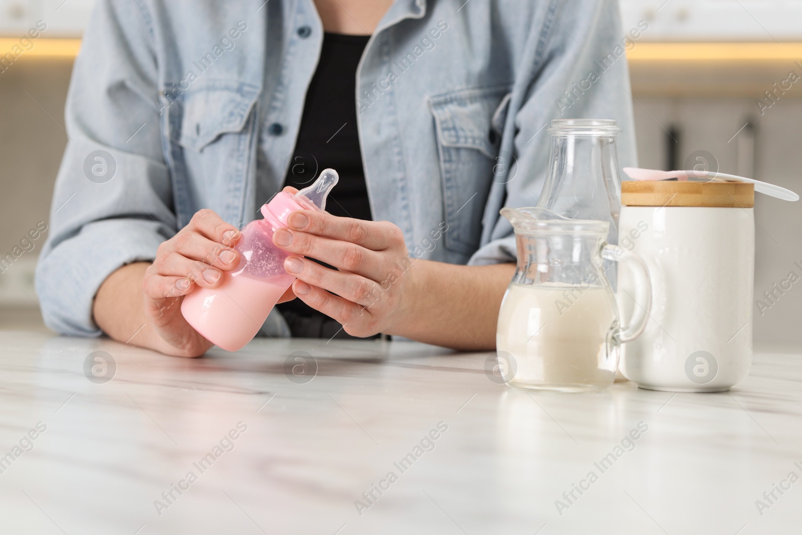 Photo of Mother making baby formula in feeding bottle at table indoors, closeup