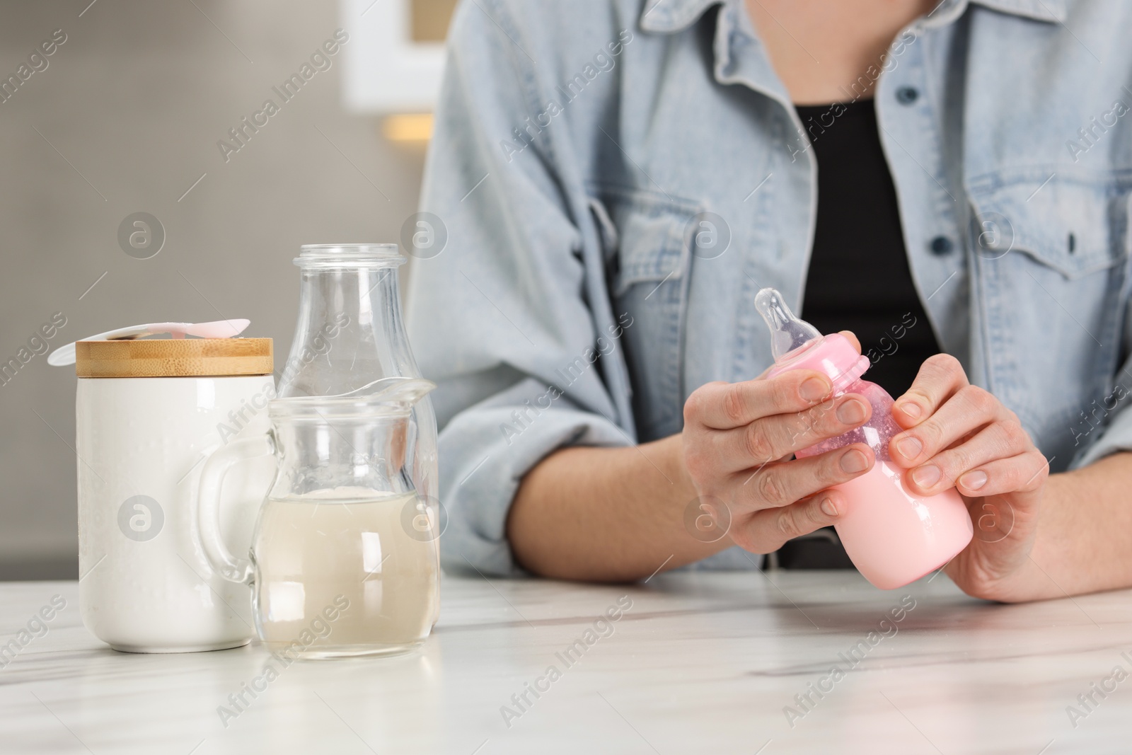 Photo of Mother making baby formula in feeding bottle at table indoors, closeup