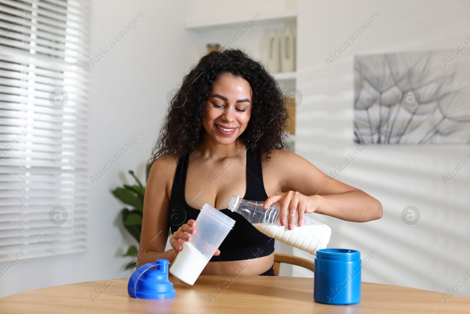 Photo of Beautiful woman making protein shake at wooden table indoors