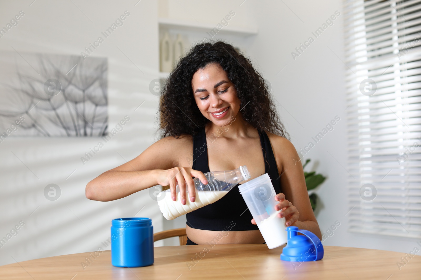 Photo of Beautiful woman making protein shake at wooden table indoors