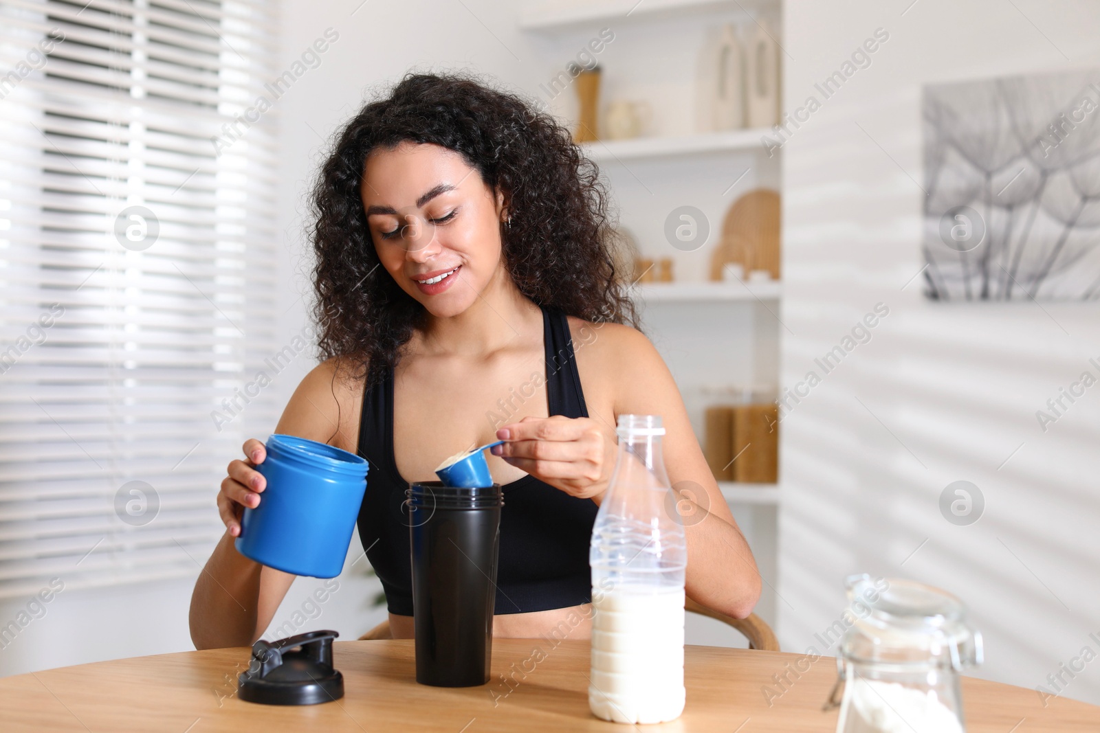 Photo of Beautiful woman making protein shake at wooden table indoors