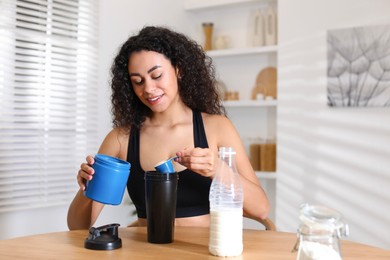 Photo of Beautiful woman making protein shake at wooden table indoors