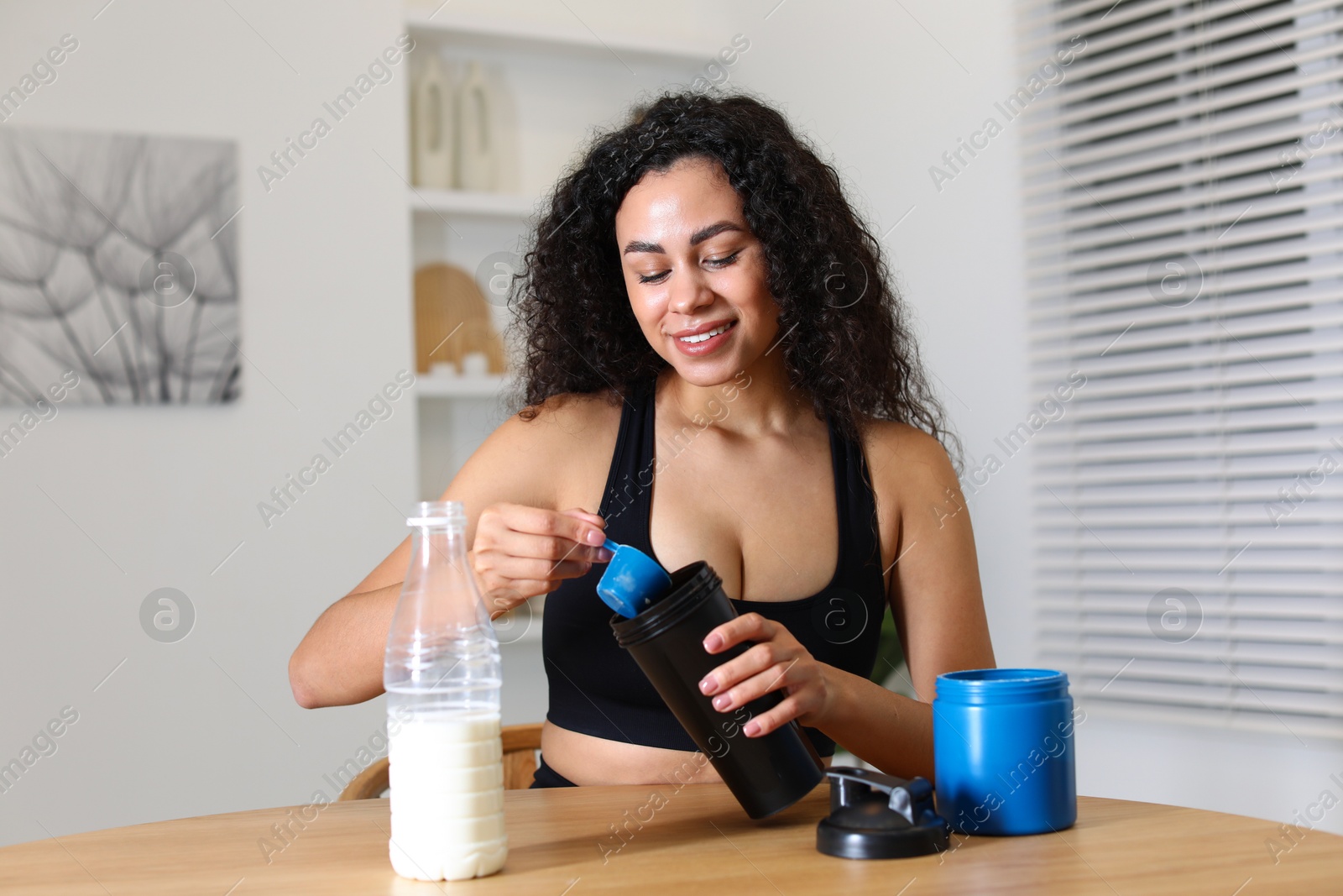 Photo of Beautiful woman making protein shake at wooden table indoors