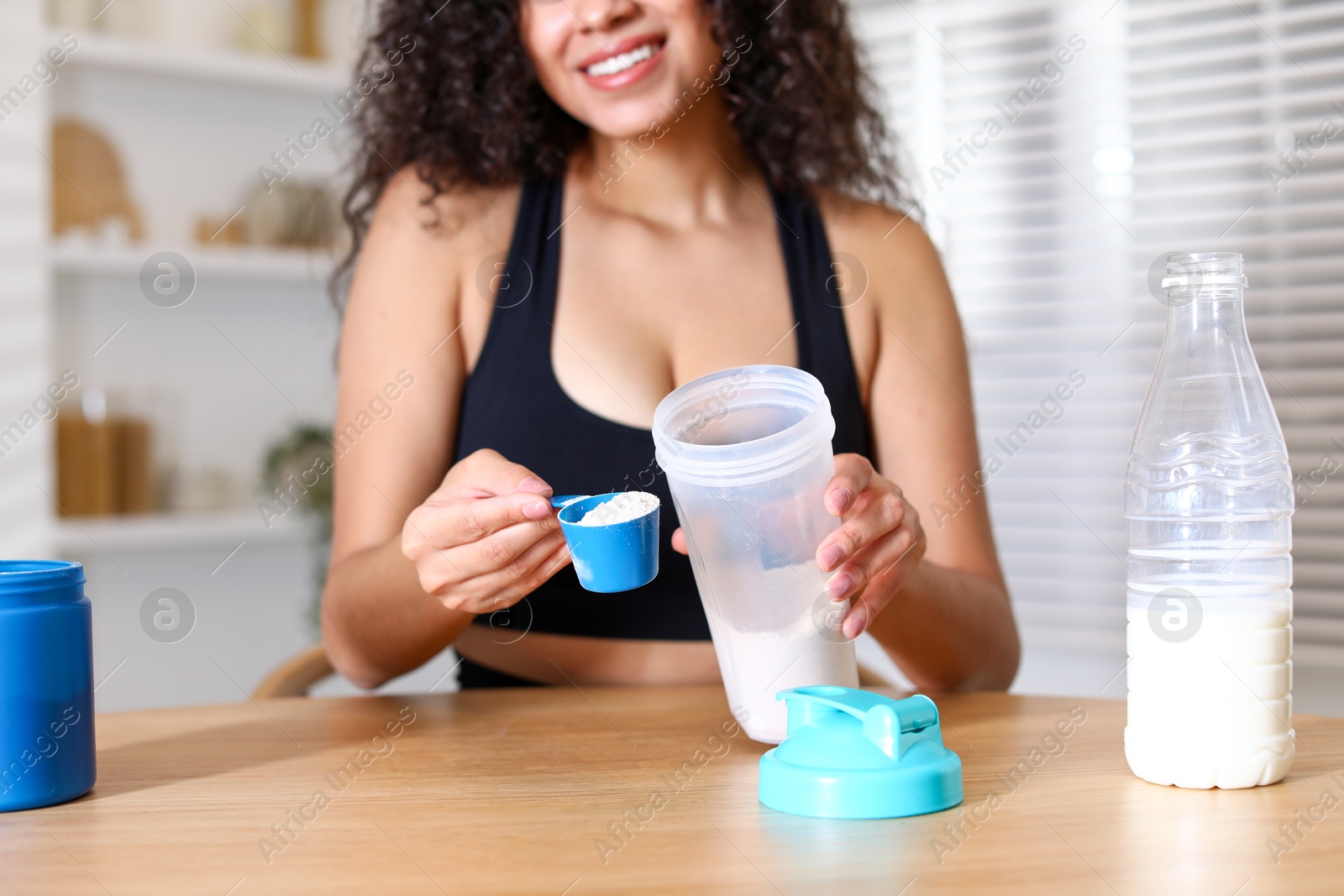 Photo of Beautiful woman making protein shake at wooden table indoors, closeup