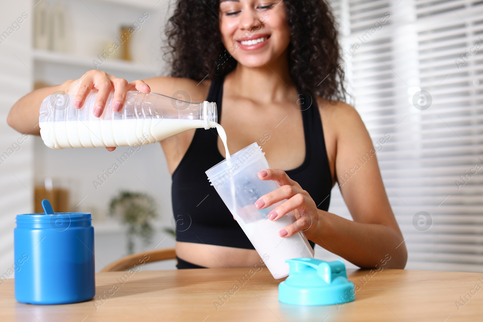 Photo of Beautiful woman making protein shake at wooden table indoors, closeup