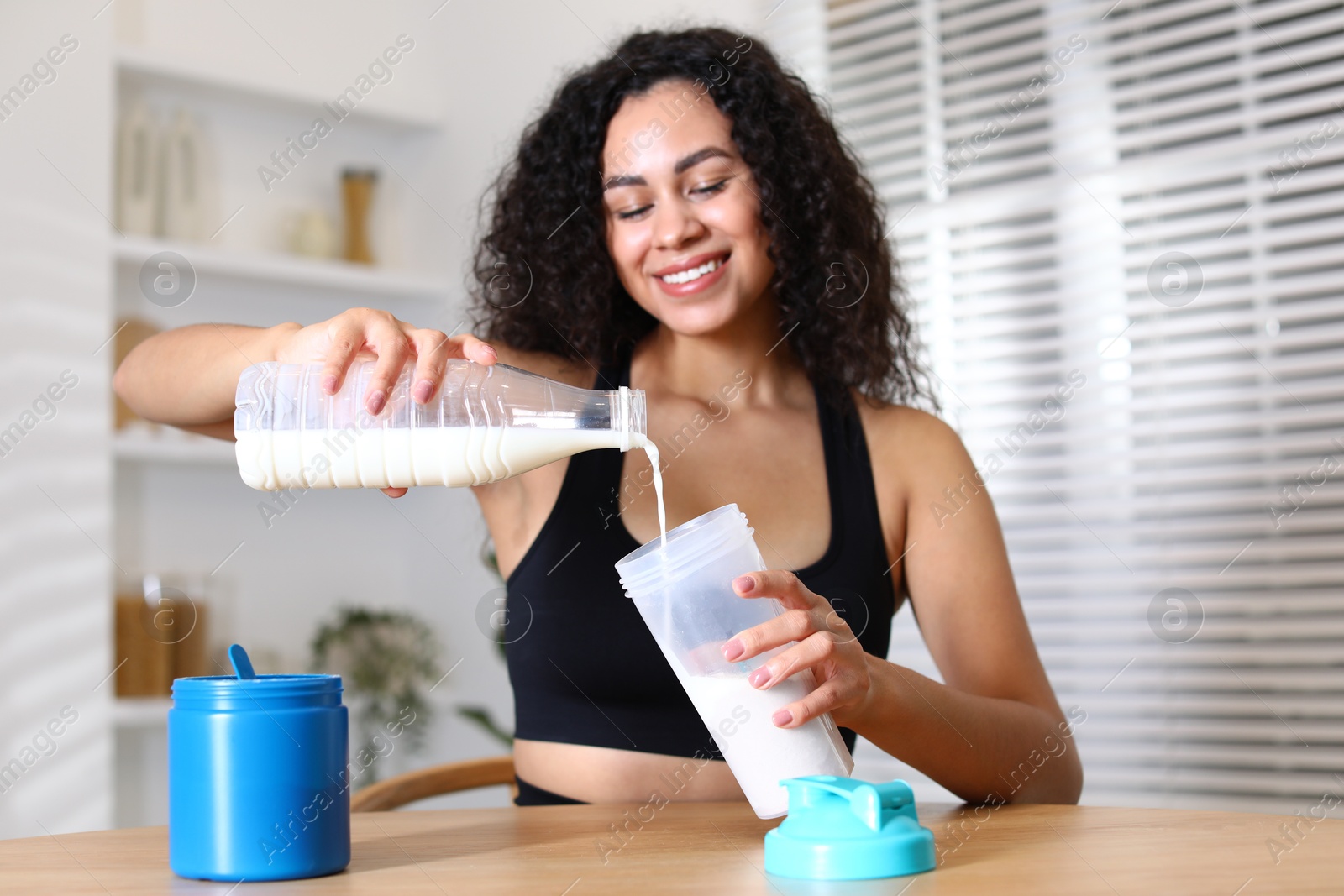 Photo of Beautiful woman making protein shake at wooden table indoors, selective focus