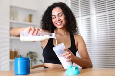 Photo of Beautiful woman making protein shake at wooden table indoors, selective focus