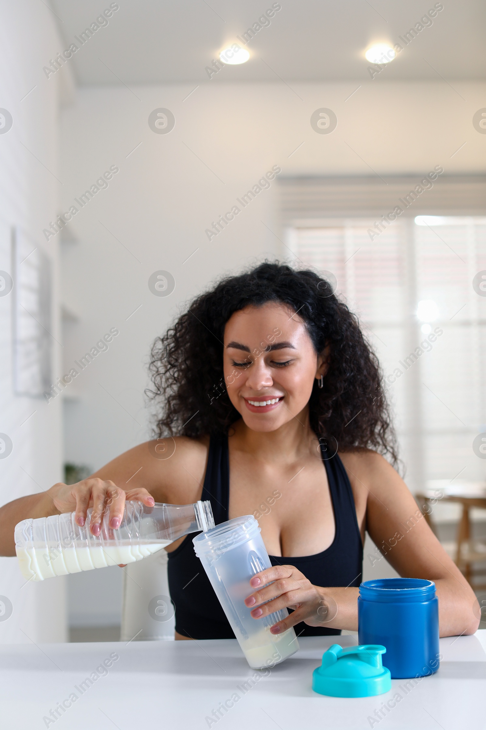 Photo of Beautiful woman making protein shake at white table indoors