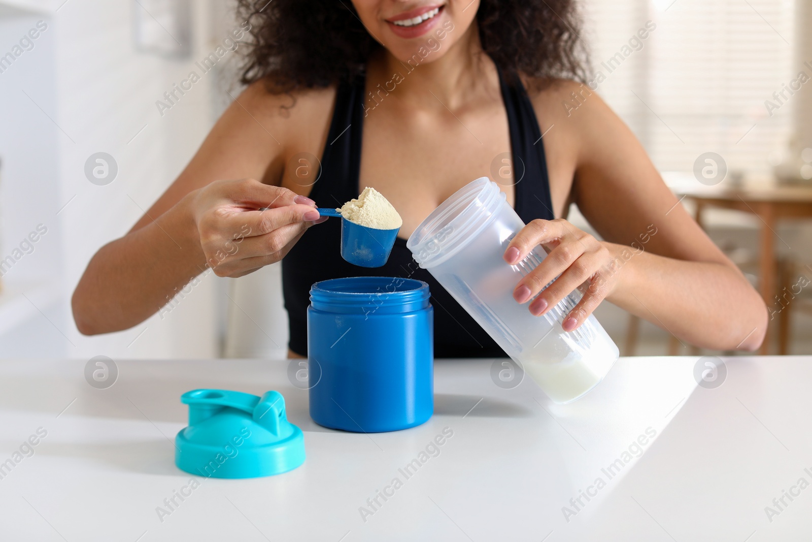 Photo of Beautiful woman making protein shake at white table indoors, closeup