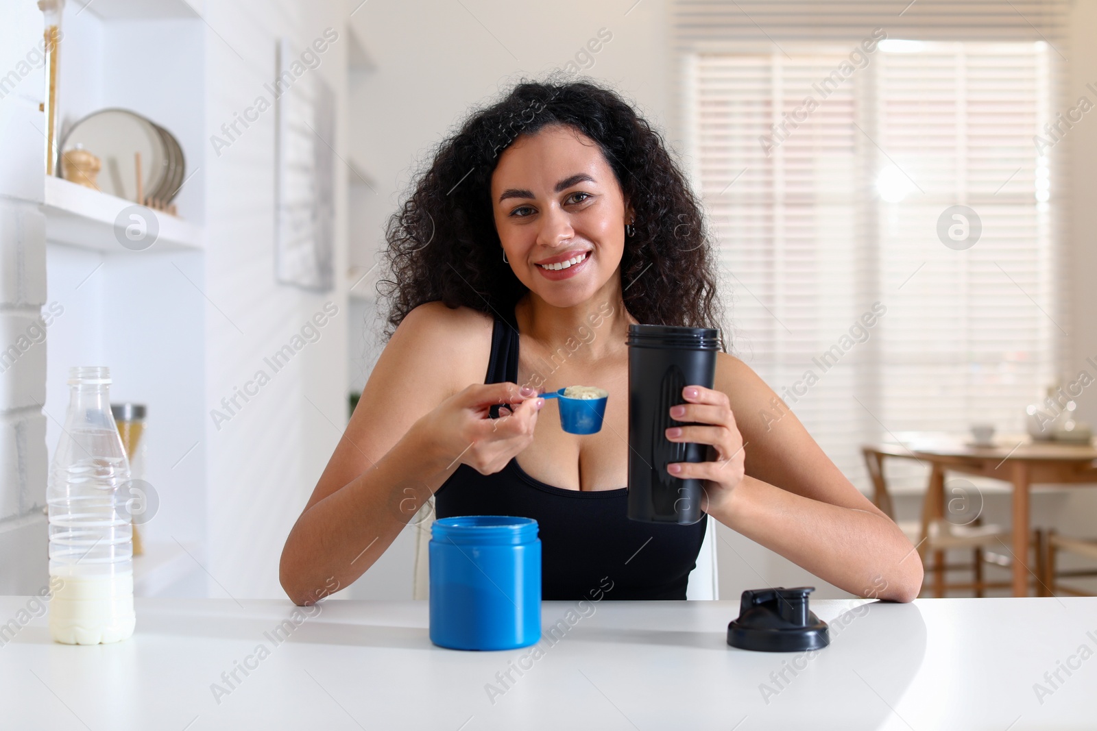 Photo of Beautiful woman making protein shake at white table indoors