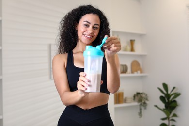 Photo of Beautiful woman with protein shake at home, selective focus