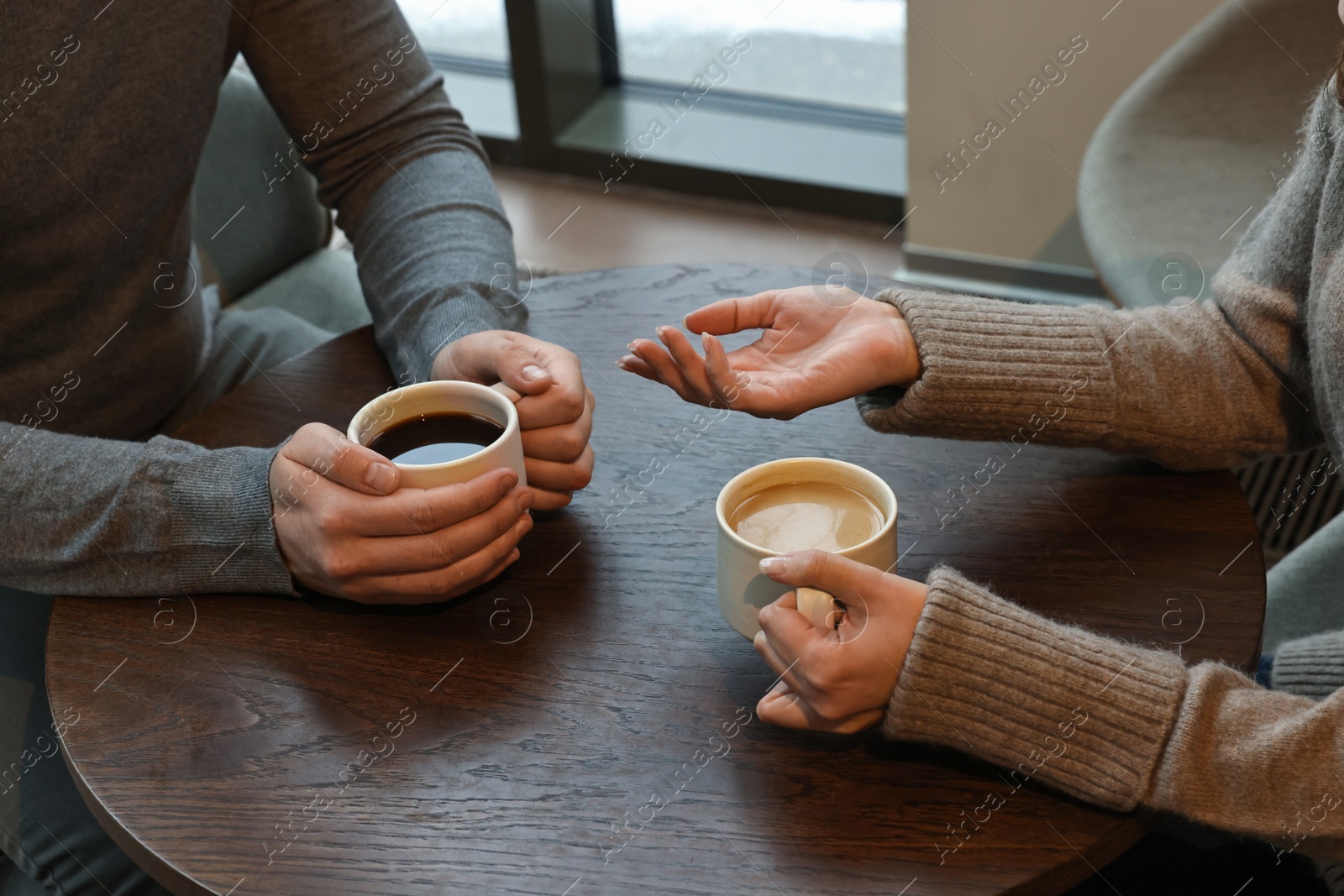 Photo of Colleagues talking during coffee break at wooden table in cafe, closeup