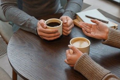 Photo of Colleagues talking during coffee break at wooden table in cafe, closeup