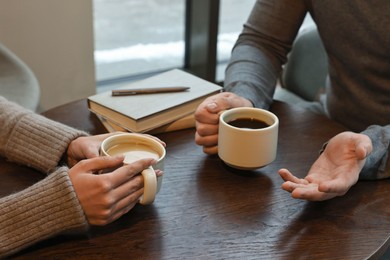 Photo of Colleagues talking during coffee break at wooden table in cafe, closeup