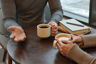 Photo of Colleagues talking during coffee break at wooden table in cafe, closeup