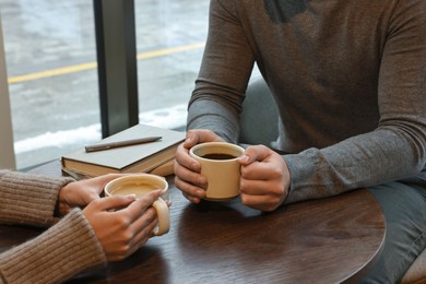 Photo of Colleagues having coffee break at wooden table in cafe, closeup