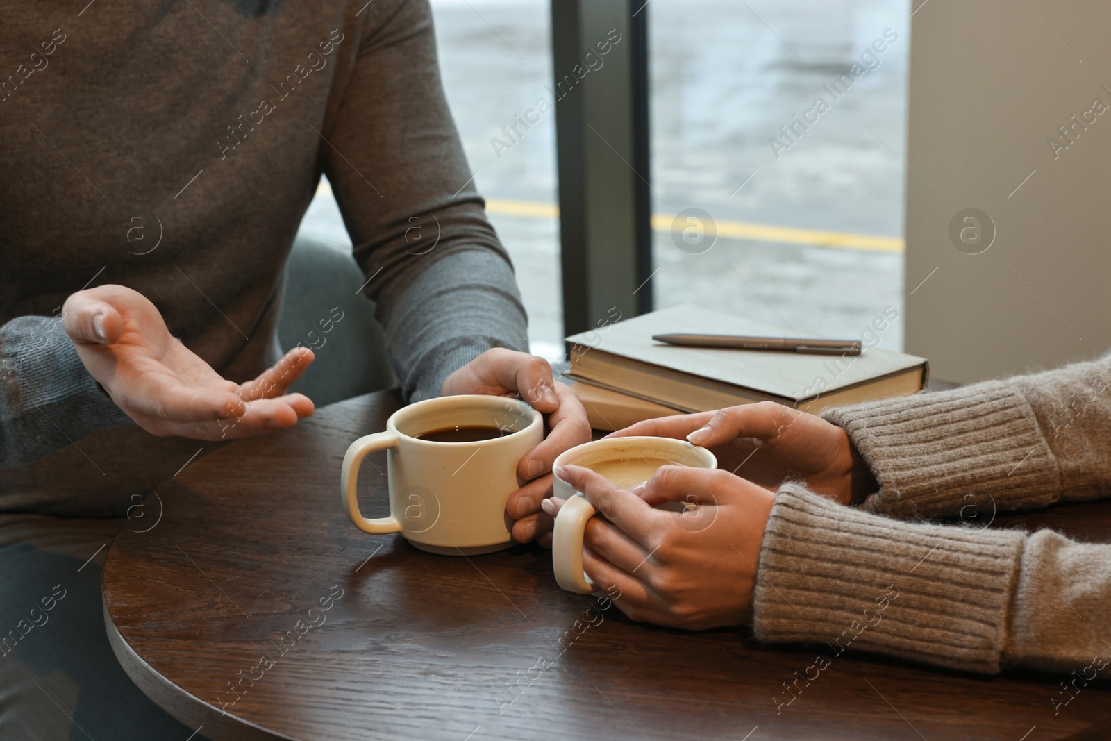 Photo of Colleagues talking during coffee break at wooden table in cafe, closeup