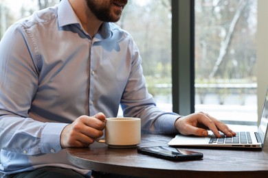 Photo of Businessman having coffee break at wooden table in cafe, closeup