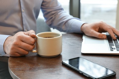 Photo of Businessman having coffee break at wooden table in cafe, closeup