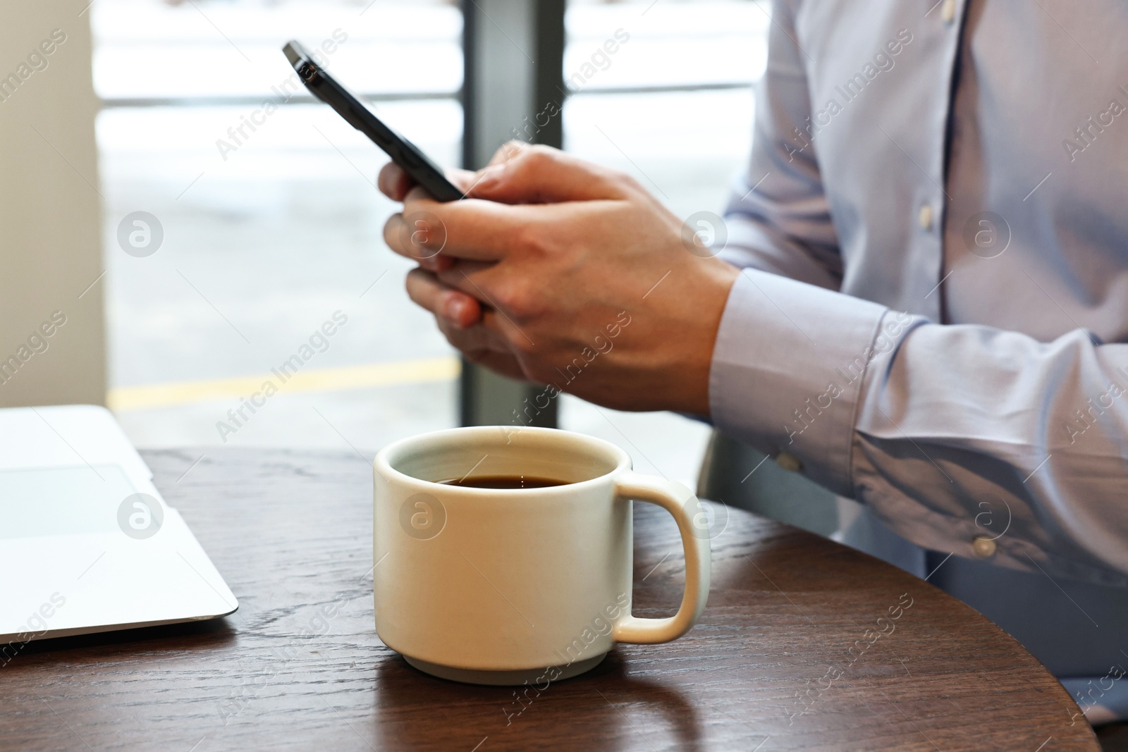 Photo of Businessman with smartphone having coffee break at wooden table in cafe, closeup