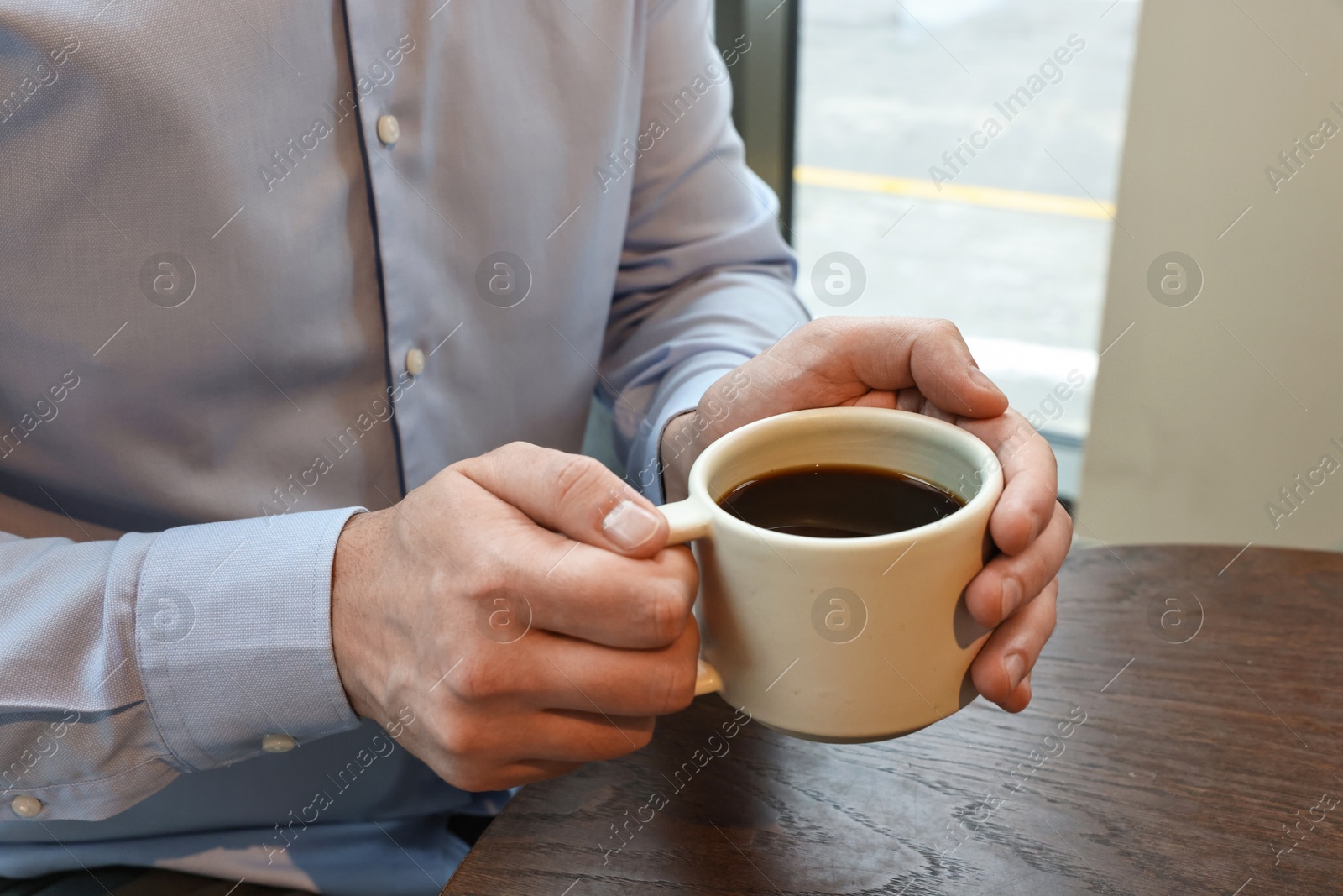 Photo of Businessman having coffee break at wooden table in cafe, closeup