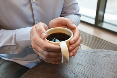 Photo of Businessman having coffee break at wooden table in cafe, closeup