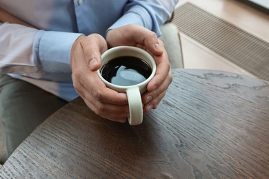 Photo of Businessman having coffee break at wooden table in cafe, closeup