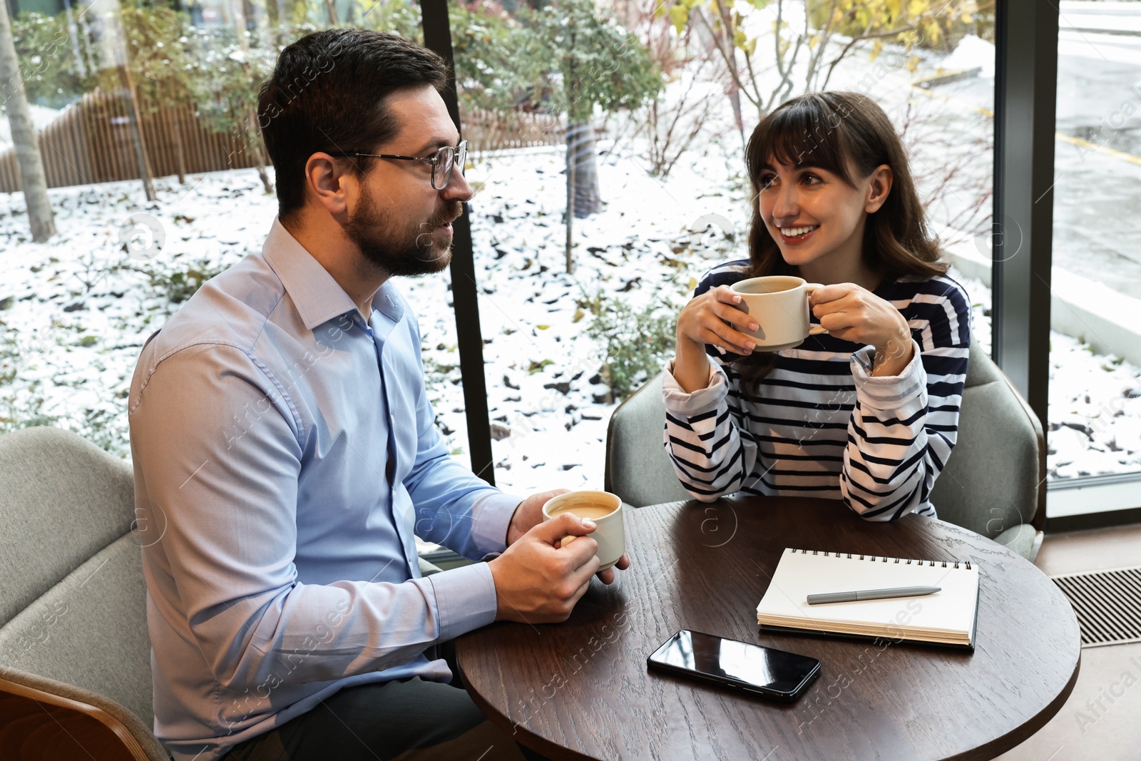 Photo of Happy colleagues talking during coffee break at wooden table in cafe