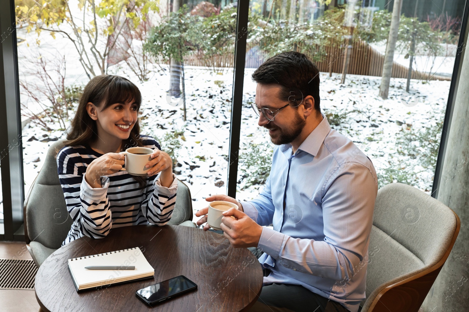 Photo of Happy colleagues talking during coffee break at wooden table in cafe