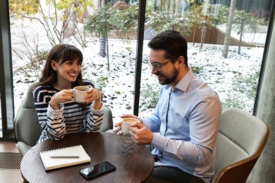 Photo of Happy colleagues talking during coffee break at wooden table in cafe