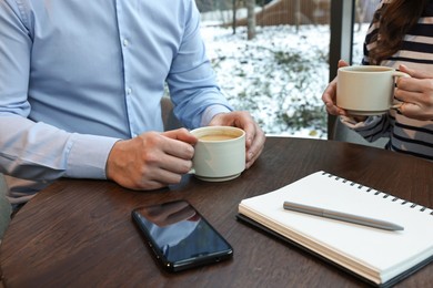 Photo of Colleagues having coffee break at wooden table in cafe, closeup