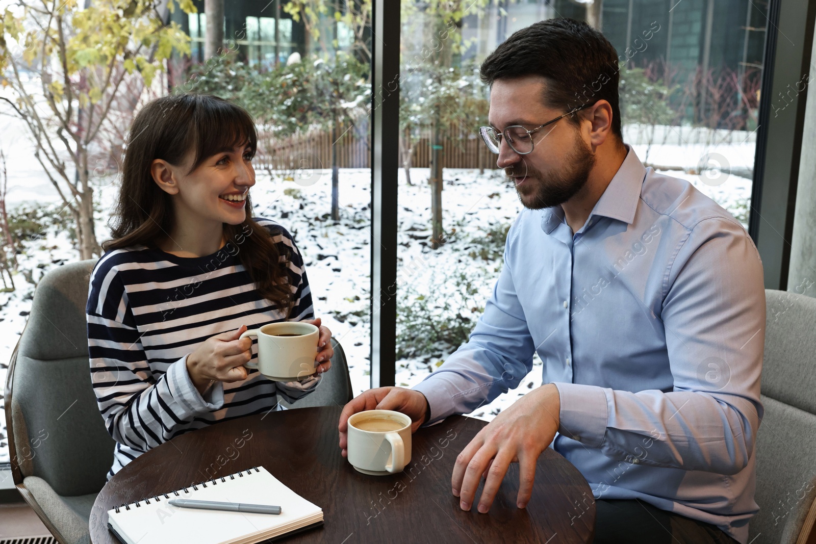 Photo of Colleagues talking during coffee break at wooden table in cafe