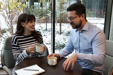 Photo of Colleagues talking during coffee break at wooden table in cafe