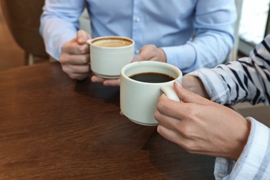 Photo of Colleagues having coffee break at wooden table in cafe, closeup