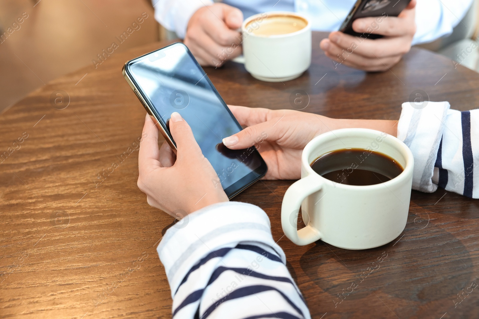 Photo of Colleagues with smartphones having coffee break at wooden table, closeup