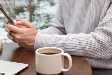 Photo of Man with smartphone having coffee break at wooden table in cafe, closeup