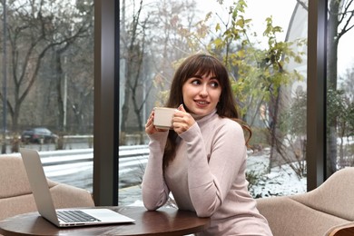 Photo of Smiling woman with laptop having coffee break at wooden table in cafe