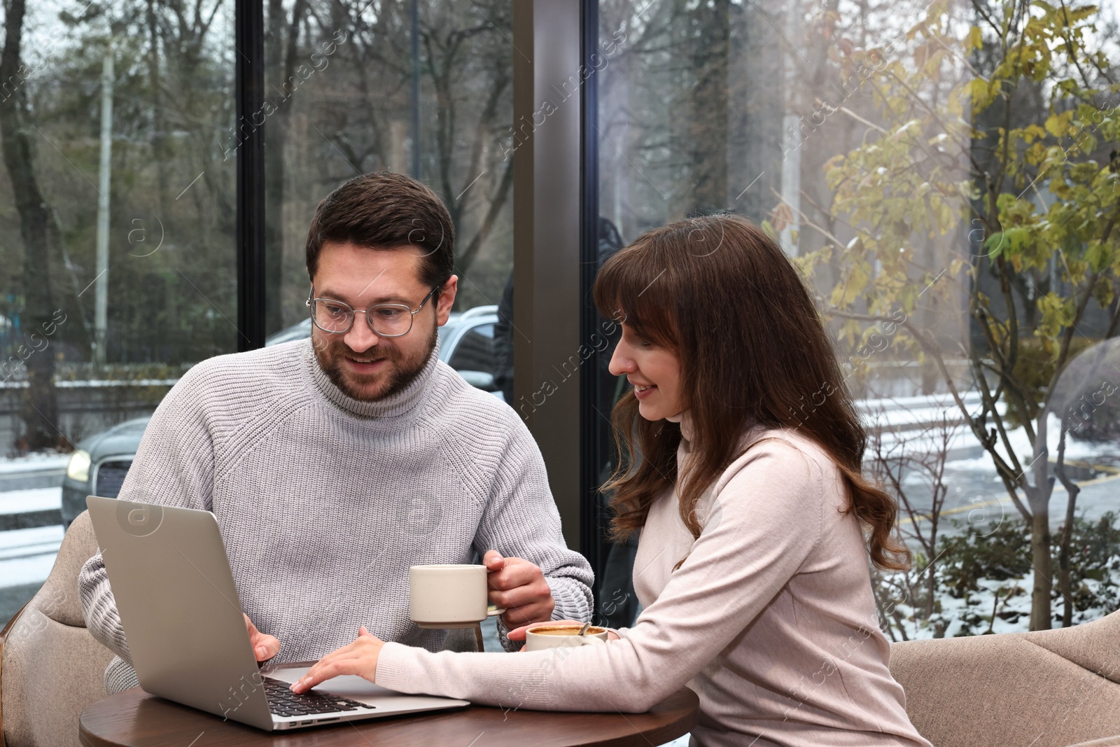 Photo of Happy colleagues using laptop during coffee break at wooden table in cafe