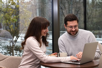 Photo of Happy colleagues using laptop during coffee break at wooden table in cafe