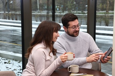 Photo of Colleagues with smartphone having coffee break at wooden table in cafe