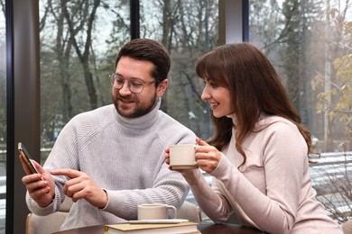 Happy colleagues with smartphone having coffee break in cafe