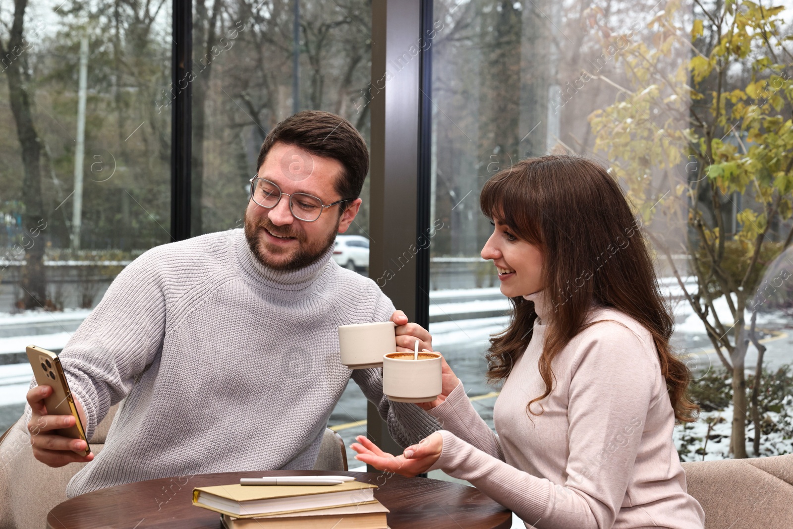 Photo of Happy colleagues with smartphone having coffee break at wooden table in cafe